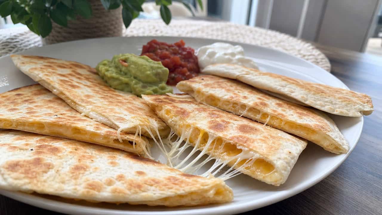 golden cheese quesadilla wedges with melty cheese pulling apart, fanned out on a wide plate on a kitchen table, natural light, shallow depth of field, landscape orientation