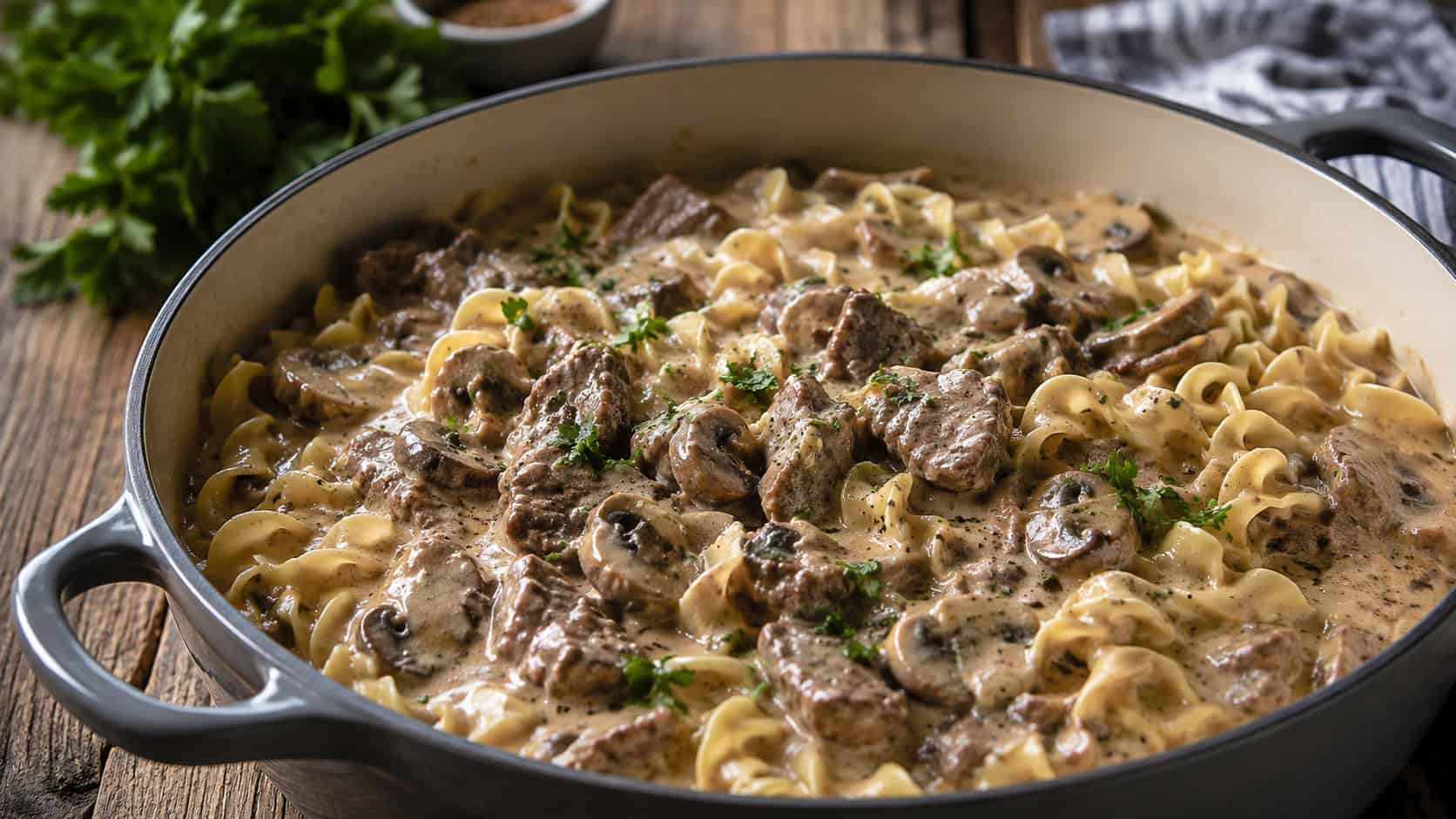 creamy beef stroganoff with egg noodles and mushrooms in a wide pot, garnished with parsley, on a rustic table, natural light, shallow depth of field, wide horizontal landscape composition