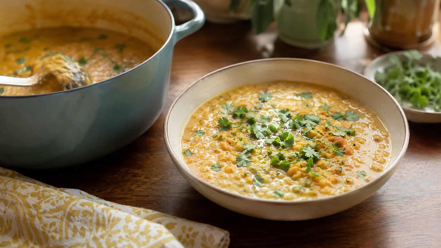 a bowl of creamy golden lentil curry topped with cilantro beside the pot, on a warm kitchen table, natural light, shallow depth of field, wide horizontal landscape composition