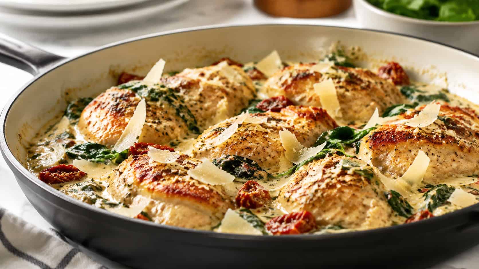 creamy Tuscan chicken with spinach and sun-dried tomatoes in a wide skillet, garnished with parmesan, on a bright kitchen counter, natural light, shallow depth of field, wide horizontal landscape composition