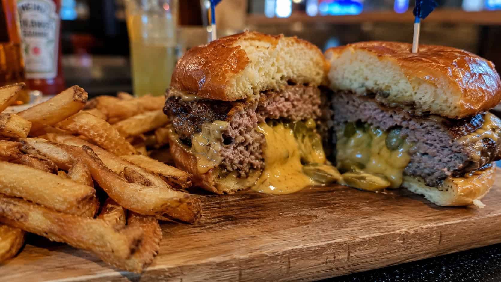 a juicy stuffed burger cut in half to reveal a molten cheesy jalapeño center, in a wide horizontal shot on a toasted bun, crispy fries piled beside it on a wooden board, casual diner setting, warm natural light, shallow depth of field, landscape orientation