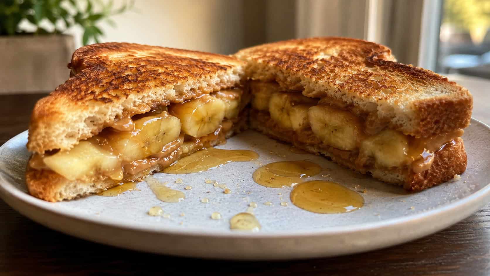 a golden grilled banana and peanut butter sandwich cut in half showing warm banana inside, honey drizzled on a plate, wide horizontal shot, warm natural light, shallow depth of field, landscape orientation