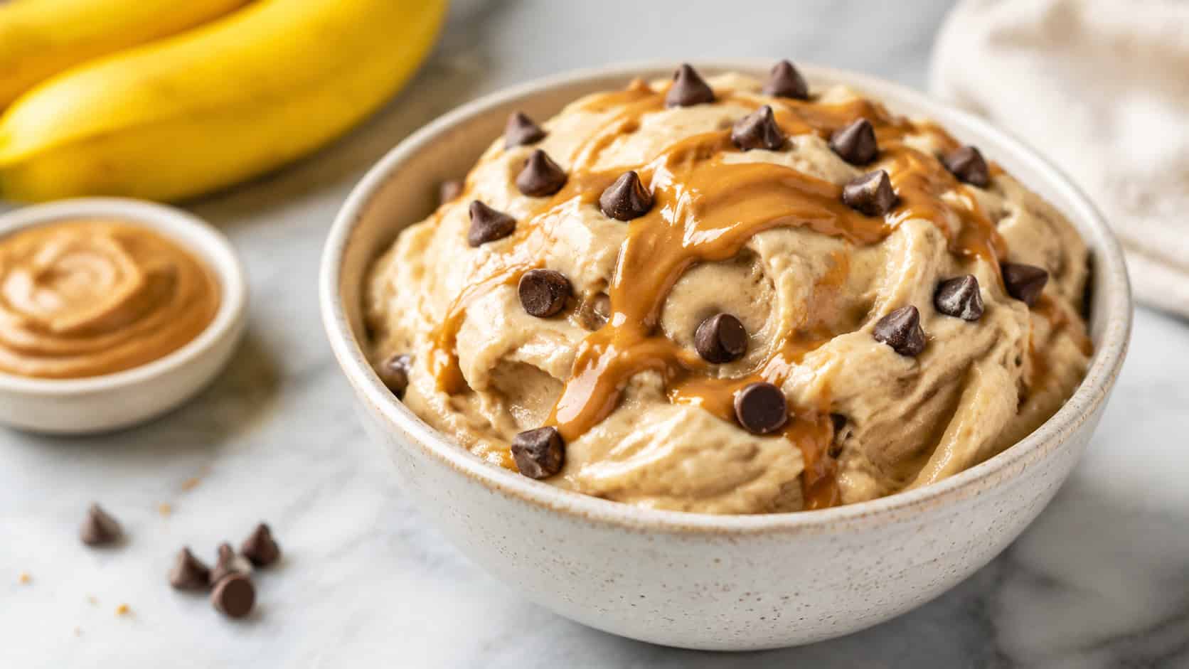 creamy banana peanut butter nice cream scooped into a bowl, swirls of peanut butter and chocolate chips on top, on a marble surface, wide horizontal shot, bright natural light, shallow depth of field, landscape orientation