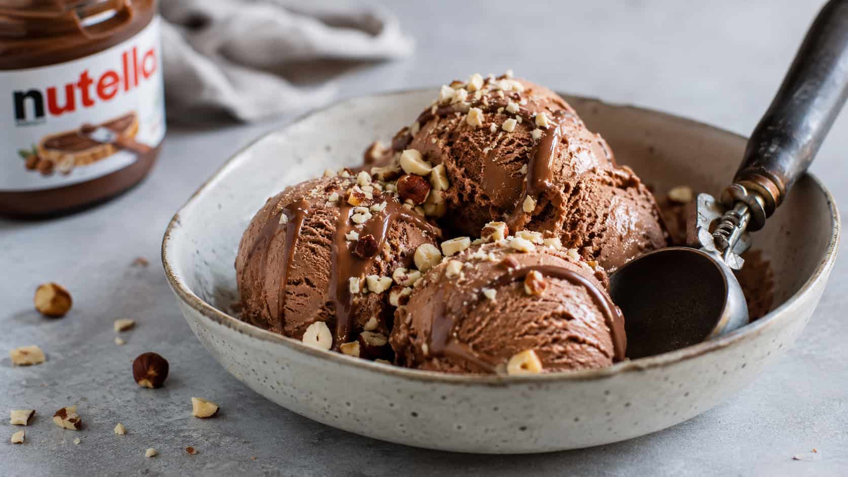 scoops of Nutella ice cream in a shallow bowl in a wide horizontal shot, creamy chocolate swirls and chopped hazelnuts, a vintage scoop resting alongside, frosty natural light, shallow depth of field, landscape orientation