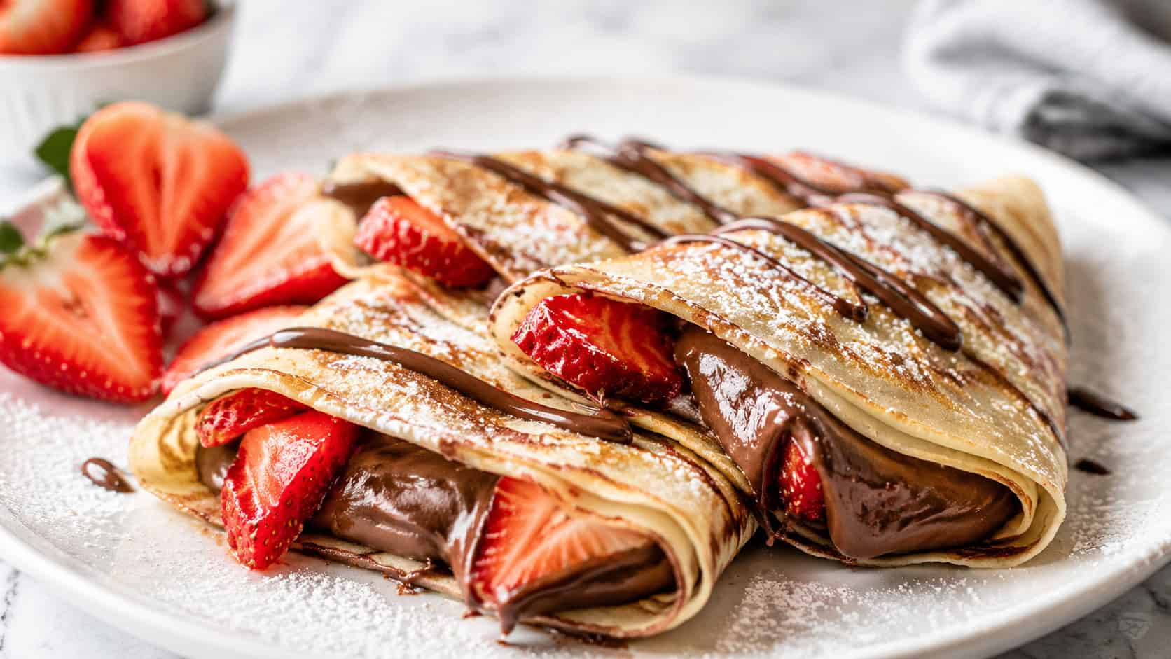 folded Nutella crepes on a plate in a wide horizontal shot, chocolate hazelnut filling peeking out, fresh strawberries and powdered sugar, a drizzle of Nutella on top, bright airy light, shallow depth of field, landscape orientation