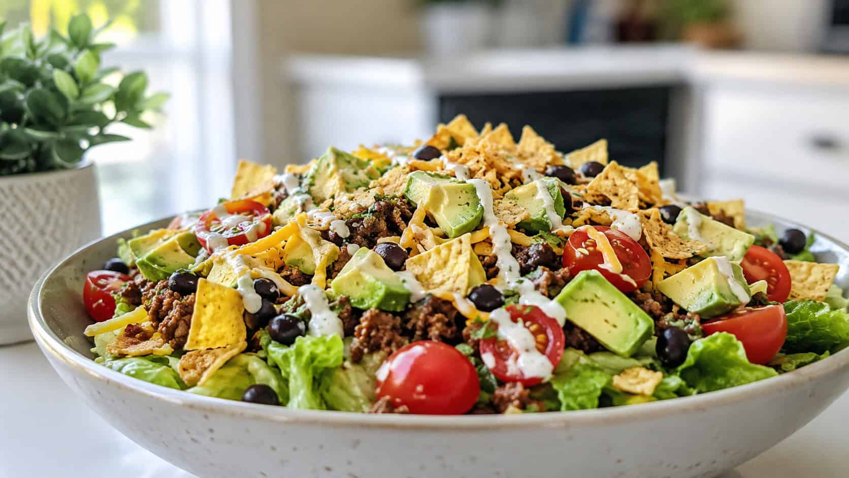 a wide bowl of taco salad piled with seasoned beef, black beans, cherry tomatoes, shredded cheese, avocado, and crushed tortilla chips, ranch drizzle on top, on a bright kitchen table, natural light, shallow depth of field, landscape orientation