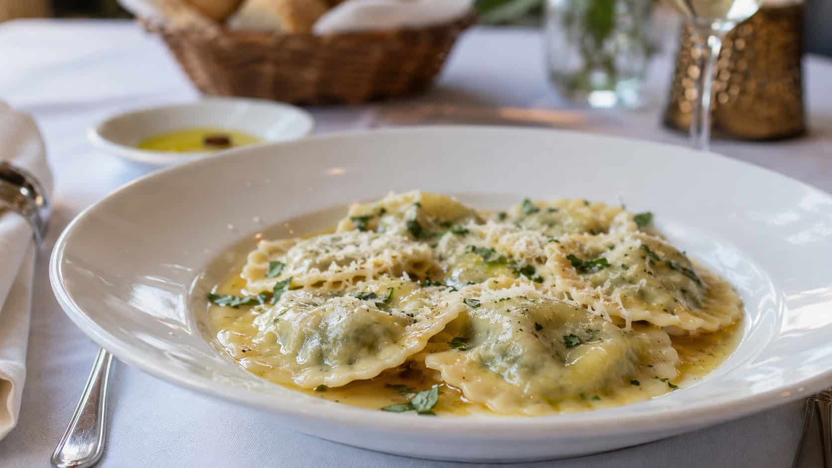 plump spinach and ricotta ravioli in a light butter sauce on a wide plate garnished with parmesan and herbs, in a wide horizontal shot, on an elegant table setting, natural light, shallow depth of field, landscape orientation