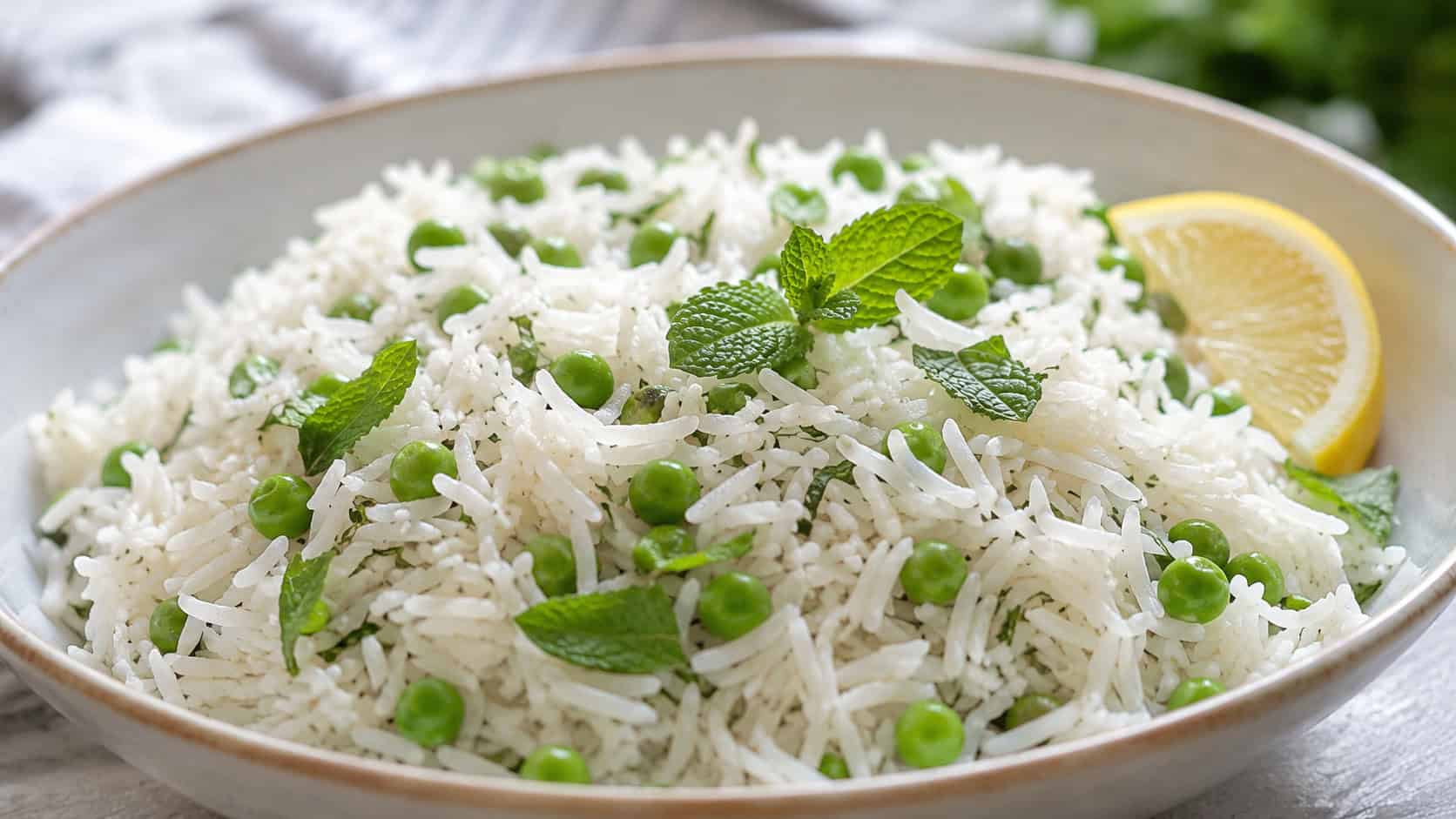 fluffy basmati rice dotted with bright green peas and fresh mint in a wide horizontal shot in a serving bowl, a lemon wedge on the side, soft natural light, shallow depth of field, landscape orientation