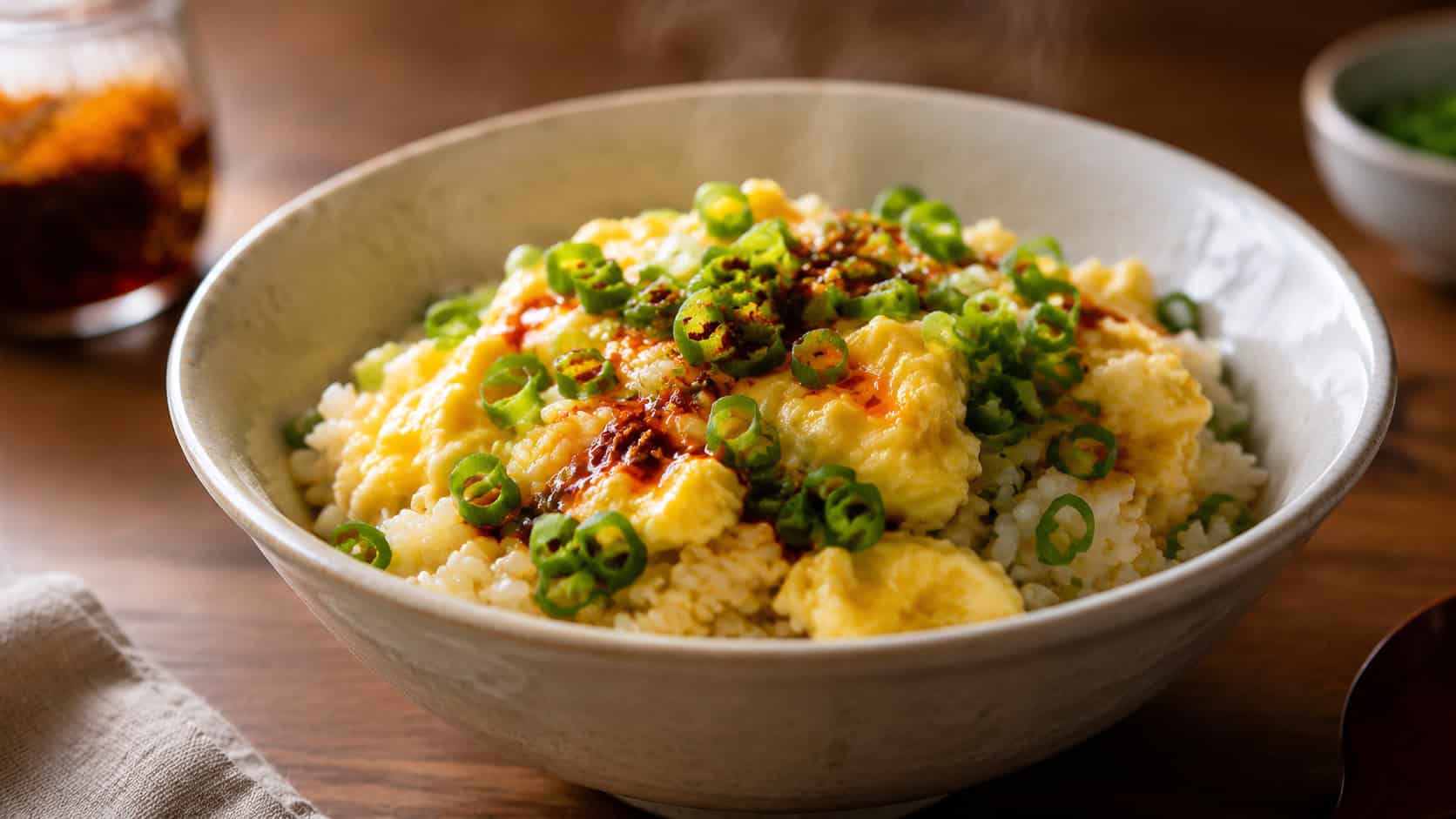 a comforting bowl of egg and scallion rice with soft scrambled egg and bright green scallions in a wide horizontal shot, a drizzle of chili oil on top, steam rising, warm natural light, shallow depth of field, landscape orientation