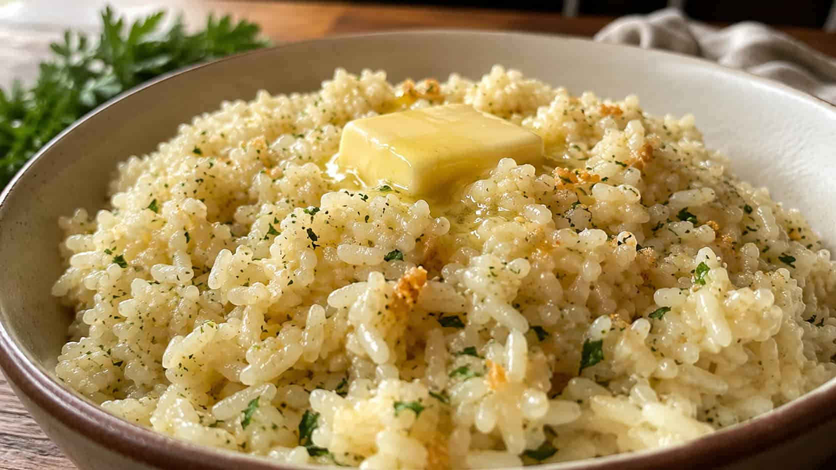 glossy garlic butter rice flecked with golden garlic and parsley in a wide horizontal shot in a bowl, a pat of butter melting on top, warm natural light, shallow depth of field, landscape orientation