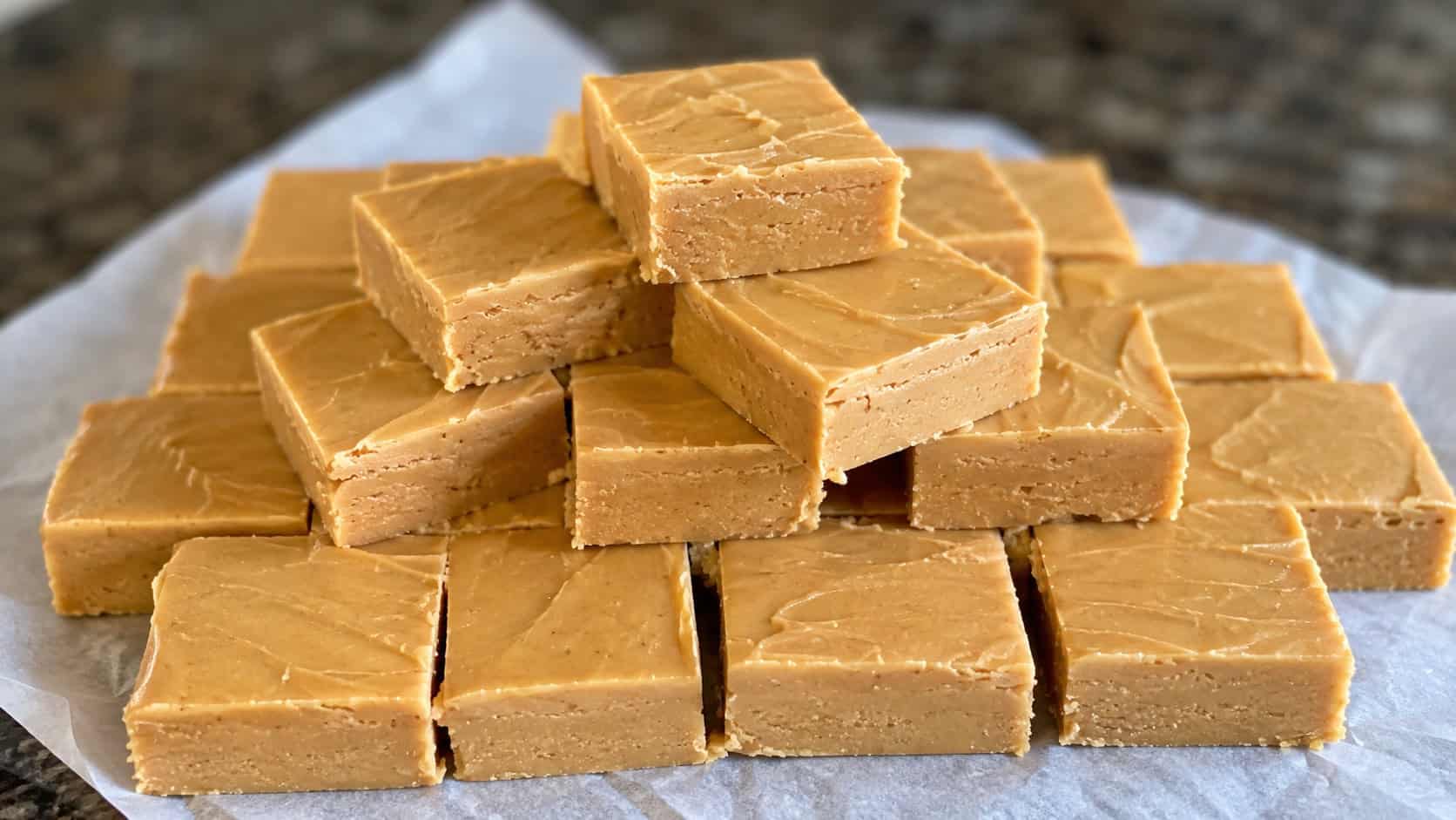 a wide board of creamy peanut butter fudge squares neatly cut and stacked, on parchment, natural light, shallow depth of field, landscape orientation