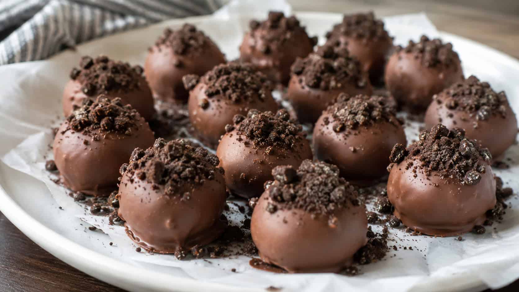 a wide platter of chocolate-coated cookie truffles topped with crushed cookie crumbs, on parchment, natural light, shallow depth of field, landscape orientation
