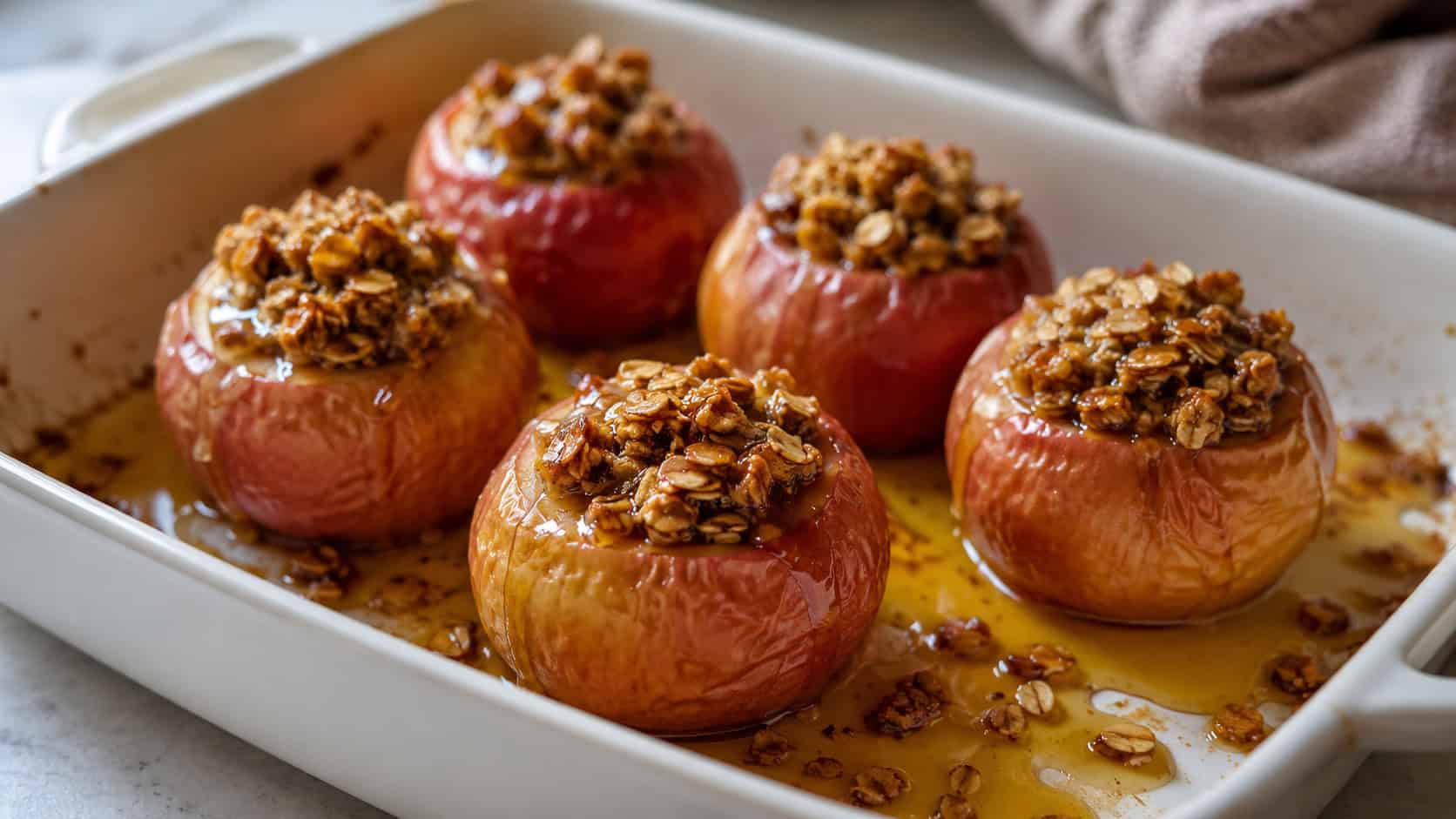 whole baked apples filled with golden granola in a wide horizontal shot, in a baking dish with glossy cider juices and a drizzle of maple, natural light, shallow depth of field, landscape orientation