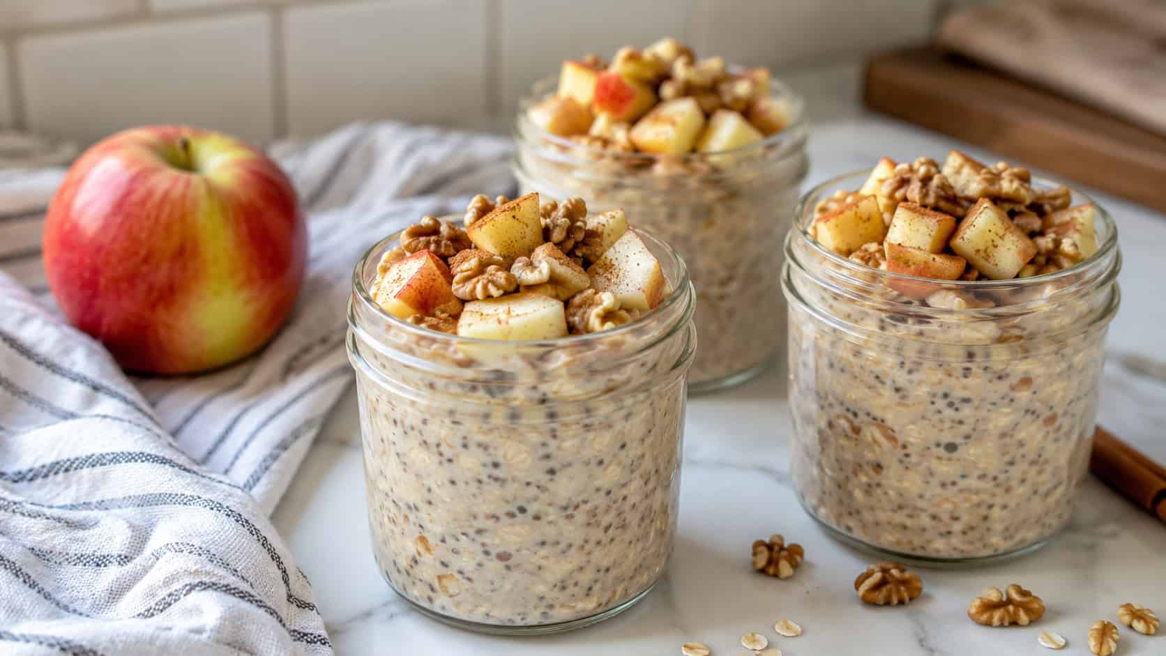 jars of creamy apple cinnamon overnight oats in a wide horizontal shot, topped with diced apple and walnuts on a bright kitchen counter, natural light, shallow depth of field, landscape orientation