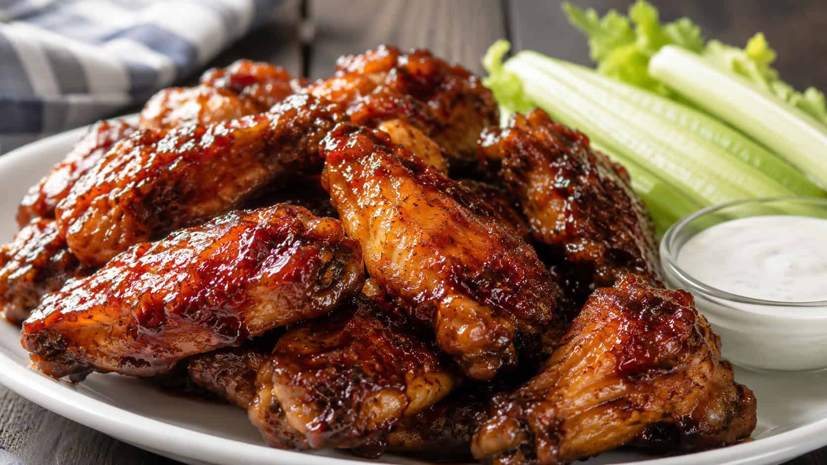 sticky glazed apple butter barbecue chicken wings in a wide horizontal shot, piled on a platter with celery sticks and a dip, natural light, shallow depth of field, landscape orientation