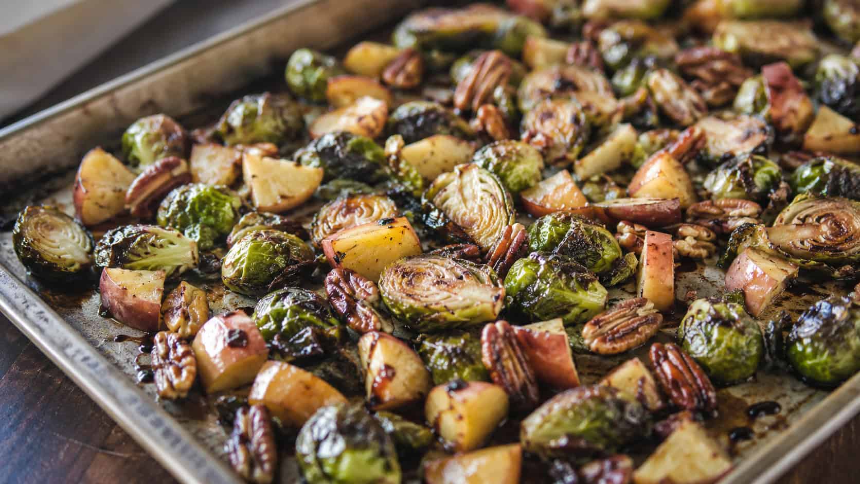roasted Brussels sprouts and caramelized apple chunks in a wide horizontal shot, on a sheet pan drizzled with balsamic and scattered with pecans, natural light, shallow depth of field, landscape orientation