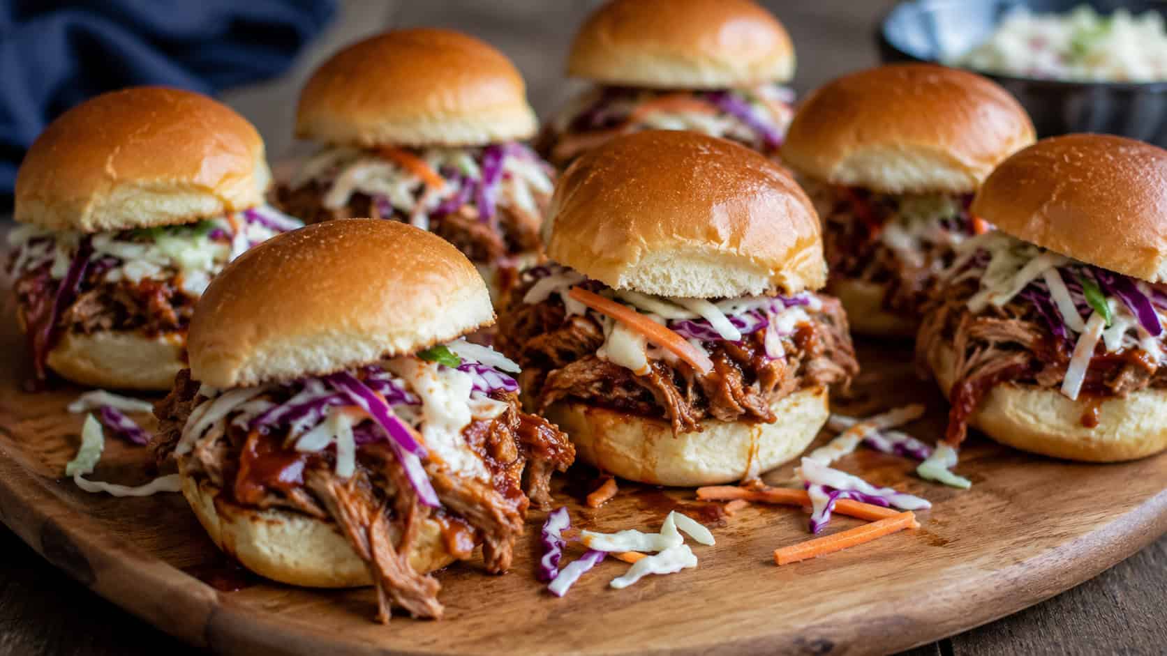 a wide platter of BBQ pulled pork sliders on soft buns with shredded saucy pork and crunchy coleslaw, on a wooden board, natural light, shallow depth of field, landscape orientation