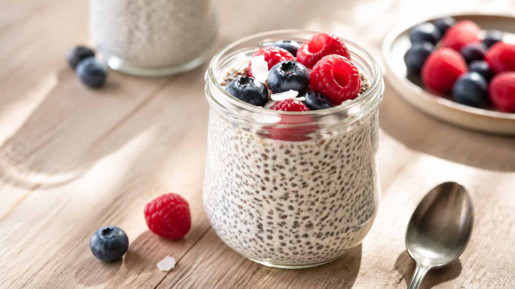 chia seed pudding in a glass jar in a wide horizontal shot, topped with fresh berries, soft creamy texture, light wooden surface, bright morning light, shallow depth of field, landscape orientation