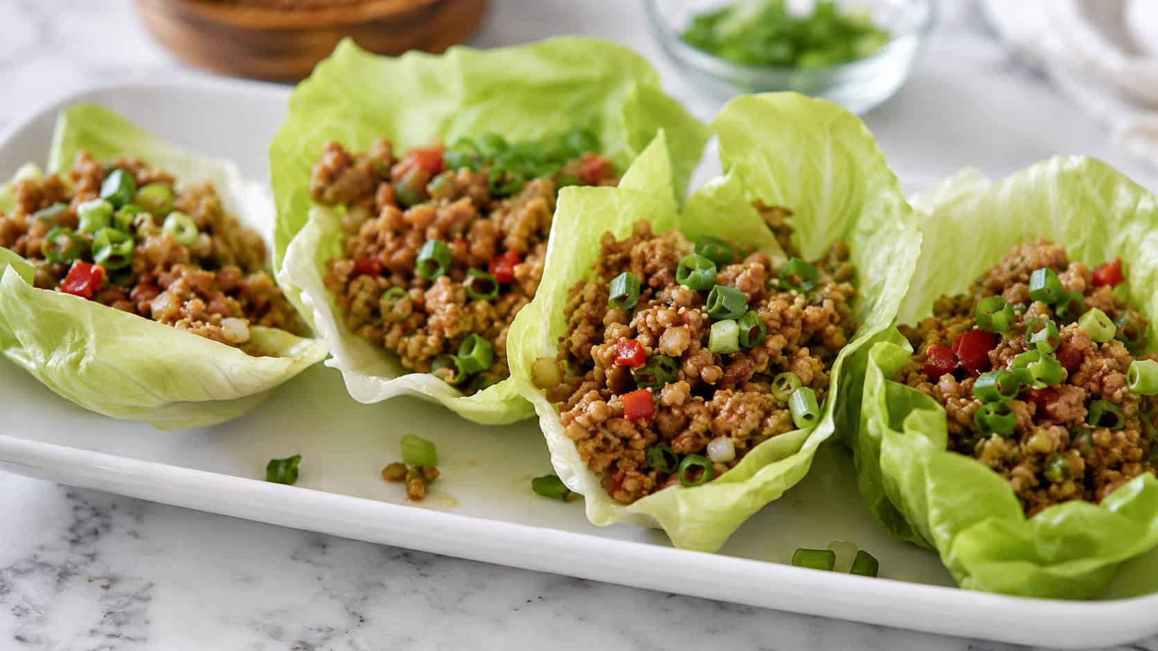 turkey lettuce wraps arranged on a white platter in a wide horizontal shot, crisp green lettuce cups, savory filling, scattered green onions, bright natural light, shallow depth of field, landscape orientation