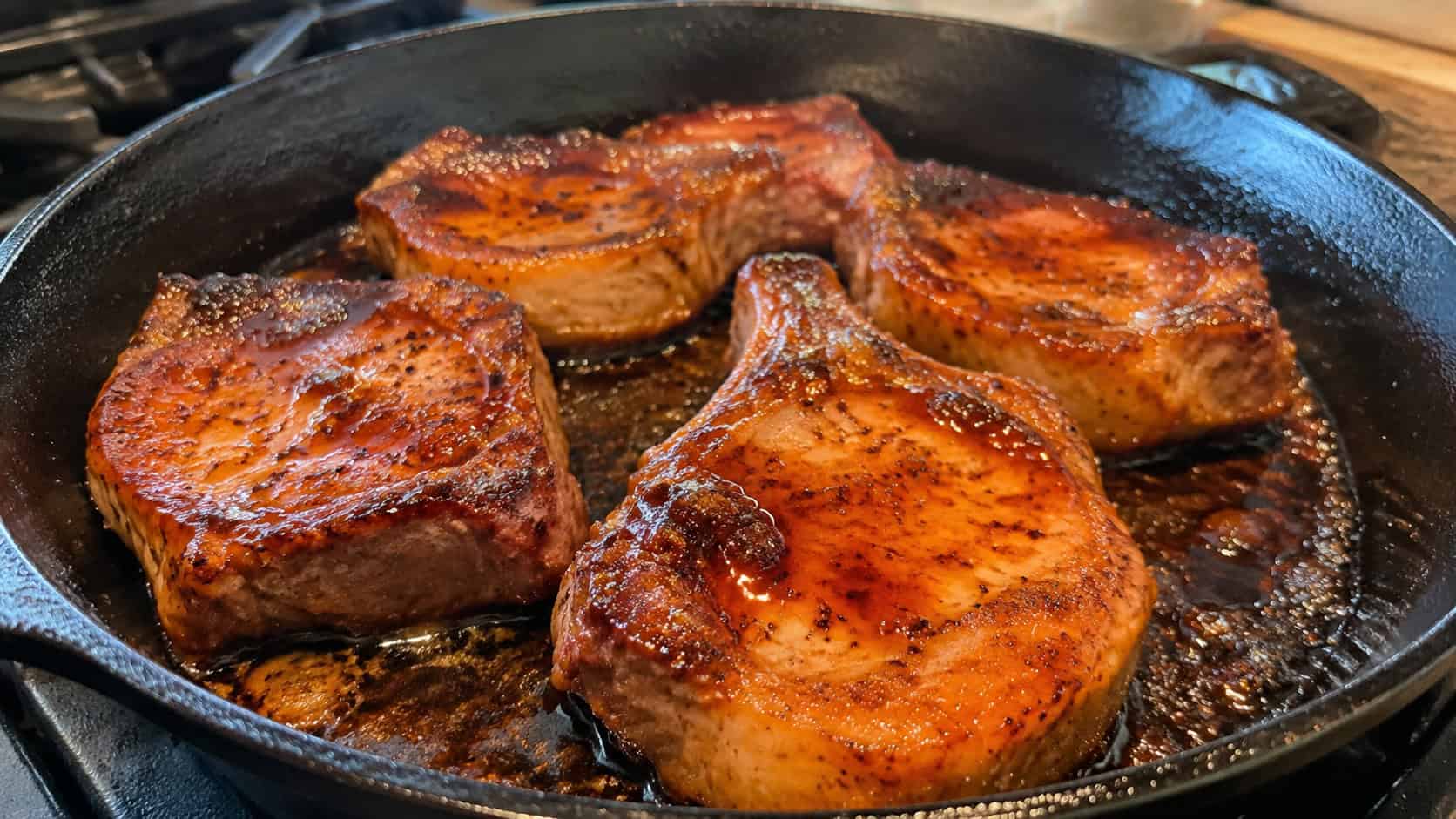 a wide horizontal skillet of glossy maple glazed pork chops with caramelized edges and a sticky sauce, on a stovetop, warm natural light, shallow depth of field, landscape orientation