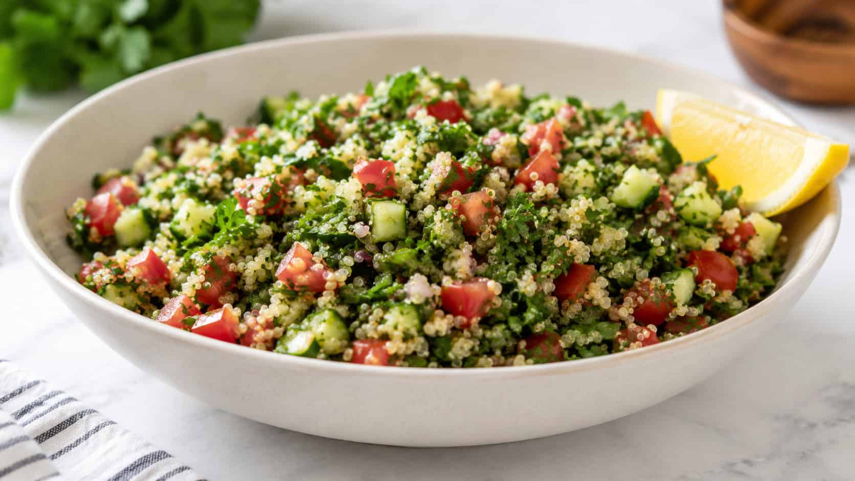a wide horizontal bowl of quinoa tabbouleh bright with green parsley, red tomato, and cucumber, lemon wedge on the rim, on a white surface, natural light, shallow depth of field, landscape orientation