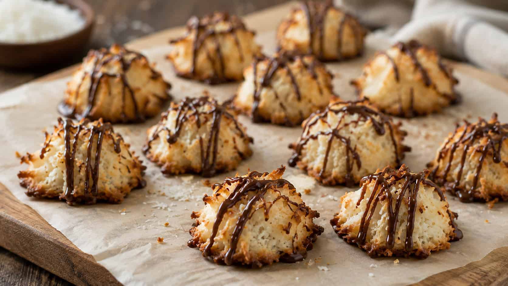 chewy coconut macaroons drizzled with chocolate in a wide horizontal shot, arranged on parchment on a wooden board, soft natural light, shallow depth of field, landscape orientation