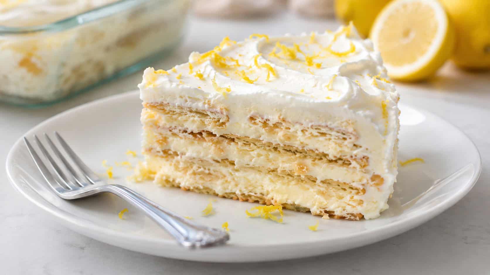 a slice of lemon icebox cake showing soft layers in a wide horizontal shot, on a white plate with lemon zest and a fork, bright natural light, shallow depth of field, landscape orientation