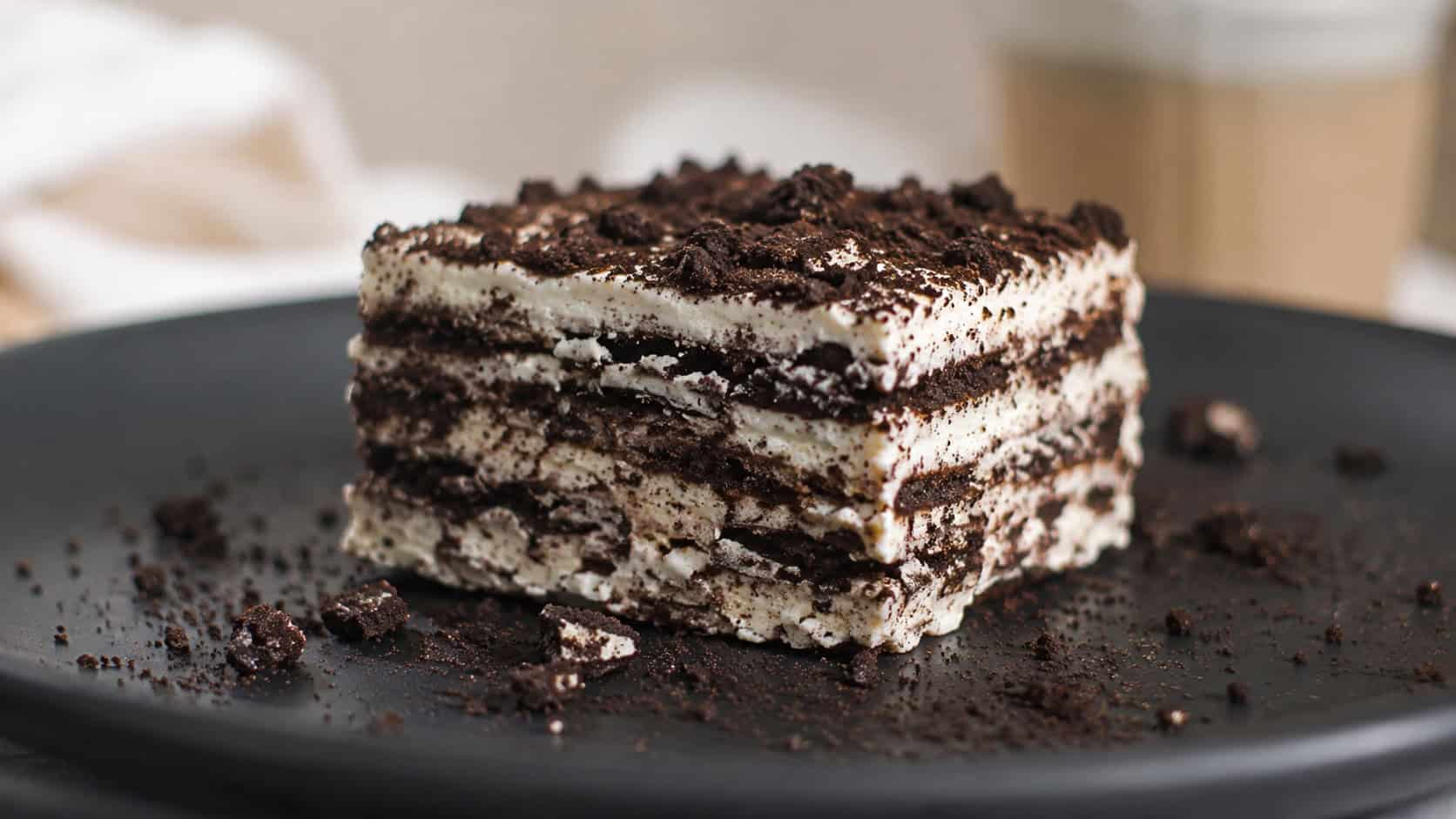 a slice of chocolate cookie icebox cake with soft layers in a wide horizontal shot, on a dark plate dusted with cookie crumbs, soft natural light, shallow depth of field, landscape orientation