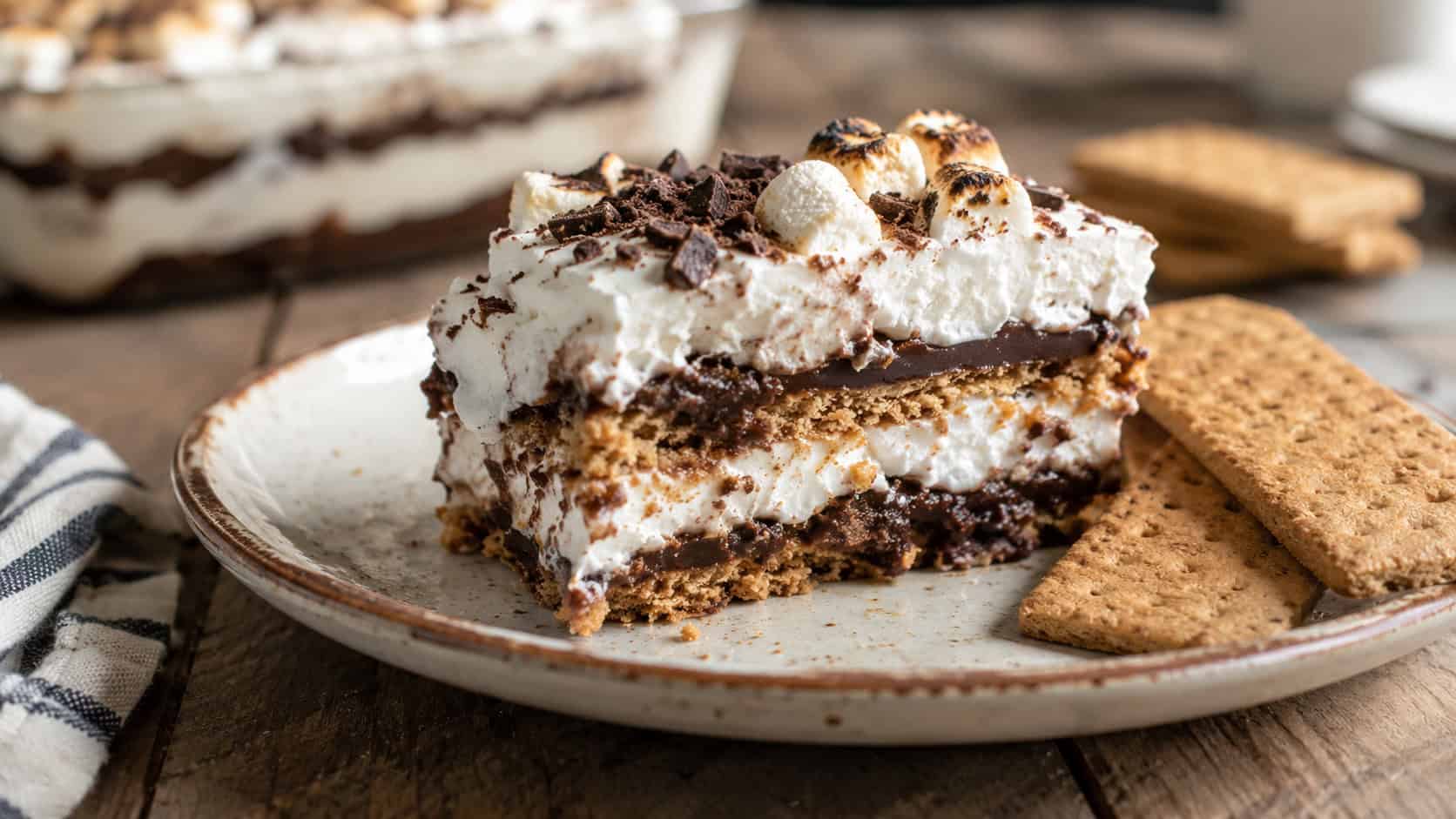 a slice of s'mores icebox cake with chocolate and marshmallow layers in a wide horizontal shot, on a rustic plate with graham crackers, warm natural light, shallow depth of field, landscape orientation