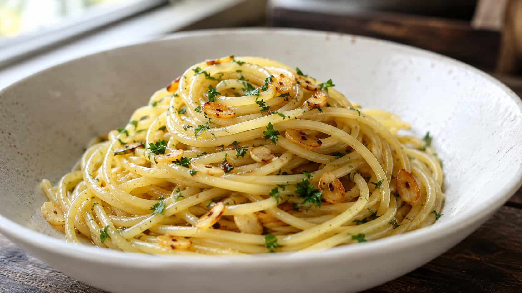 pasta aglio e olio in a wide horizontal shot, a twirled nest of glossy spaghetti with golden garlic and green parsley in a shallow bowl, natural light, shallow depth of field, landscape orientation