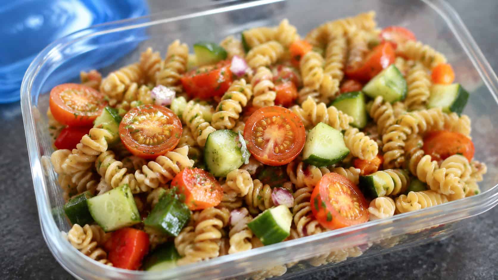 a gluten-free brown rice pasta salad in a wide horizontal shot, colorful pasta with tomatoes and cucumber in a lunch container, bright natural light, shallow depth of field, landscape orientation