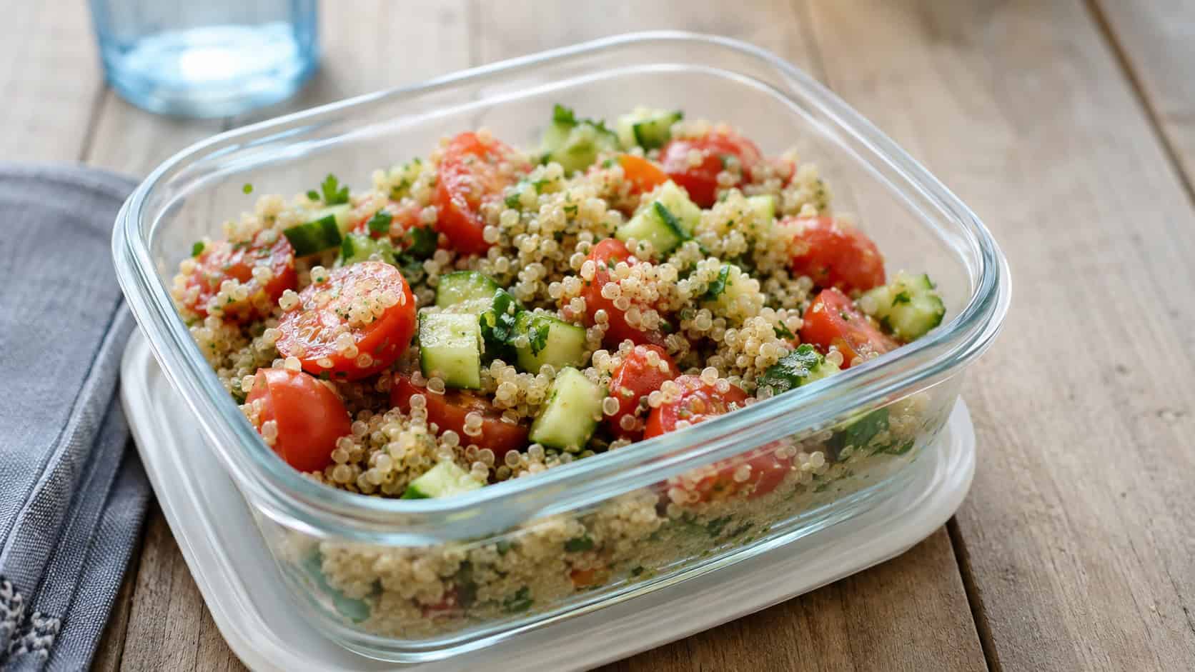 a fresh quinoa salad with halved cherry tomatoes and diced cucumber in a small lunch container, in a wide horizontal shot, bright natural light, shallow depth of field, landscape orientation