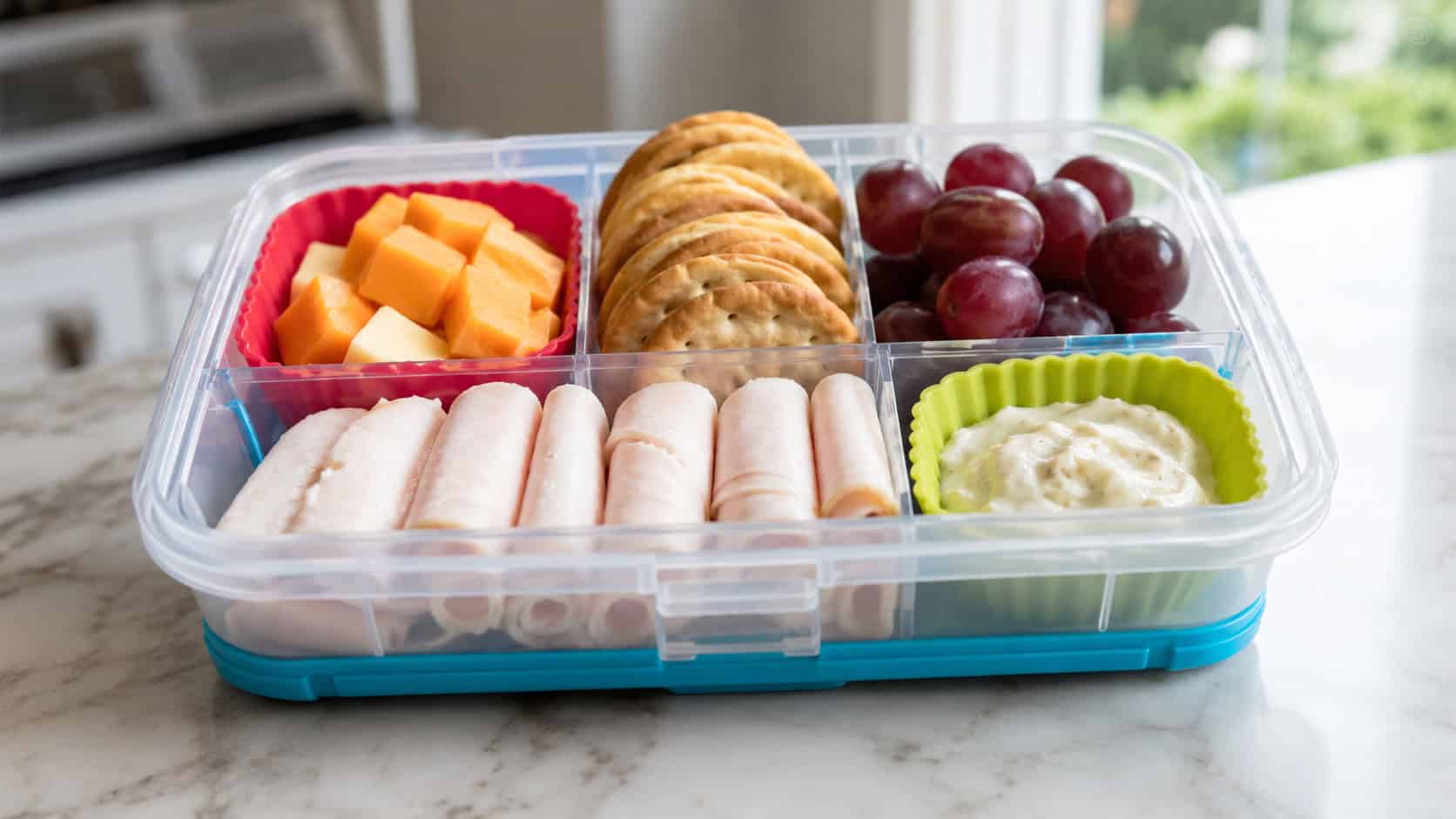 a colorful bento box in a wide horizontal shot, with neat compartments of cheese cubes, crackers, grapes, and rolled turkey on a bright counter, natural light, shallow depth of field, landscape orientation