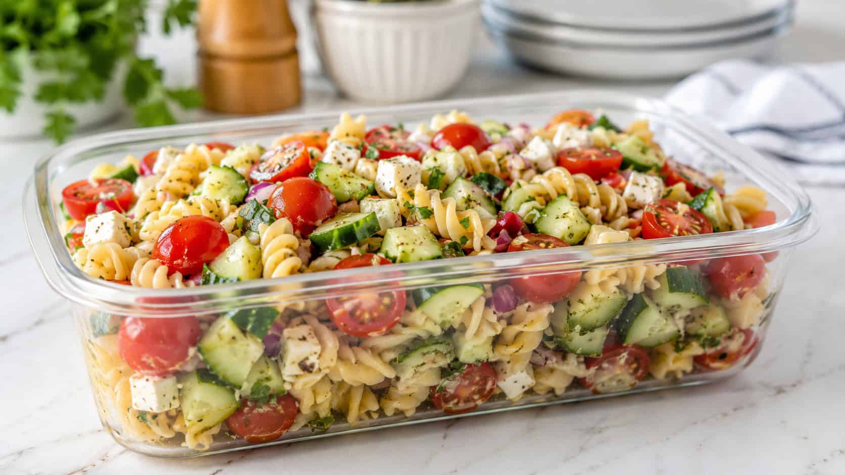 a colorful pasta salad with tomatoes, cucumber, and cheese in a wide horizontal lunch container, set on a bright kitchen table, natural light, shallow depth of field, landscape orientation