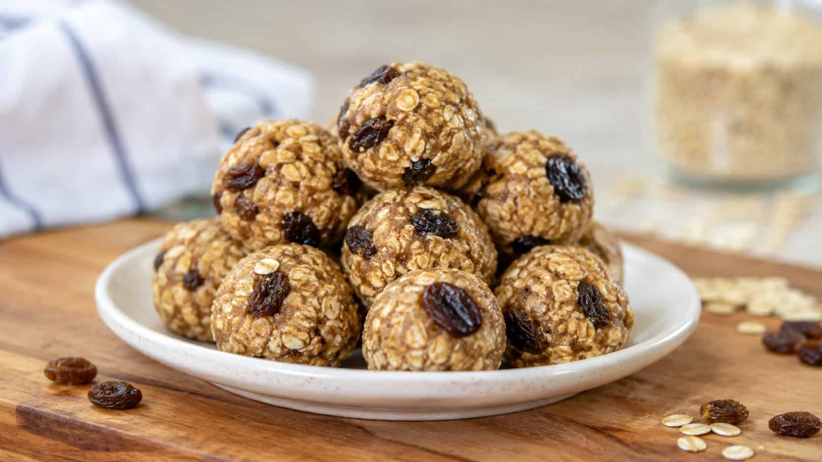 a cluster of round oatmeal raisin energy bites piled on a small plate, dotted with plump raisins, in a wide horizontal shot on a wooden board, natural light, shallow depth of field, landscape orientation