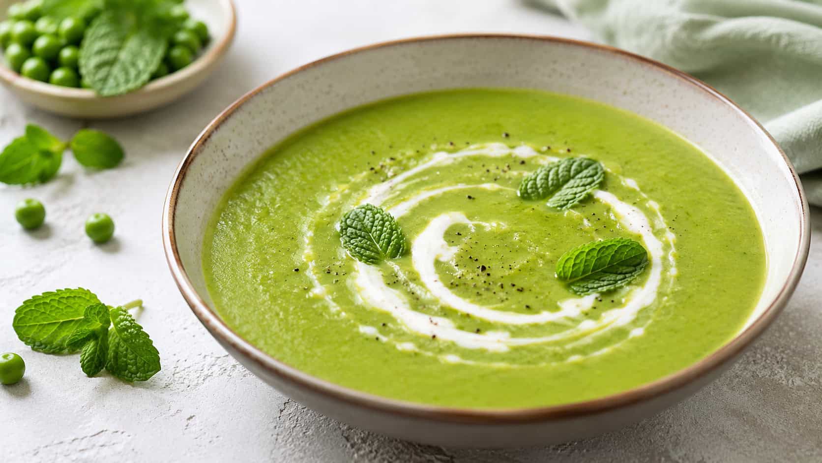 a bowl of vibrant green pea and mint soup in a wide horizontal shot, bright green and smooth with a swirl of cream and mint leaves, on a light table, fresh natural light, shallow depth of field, landscape orientation
