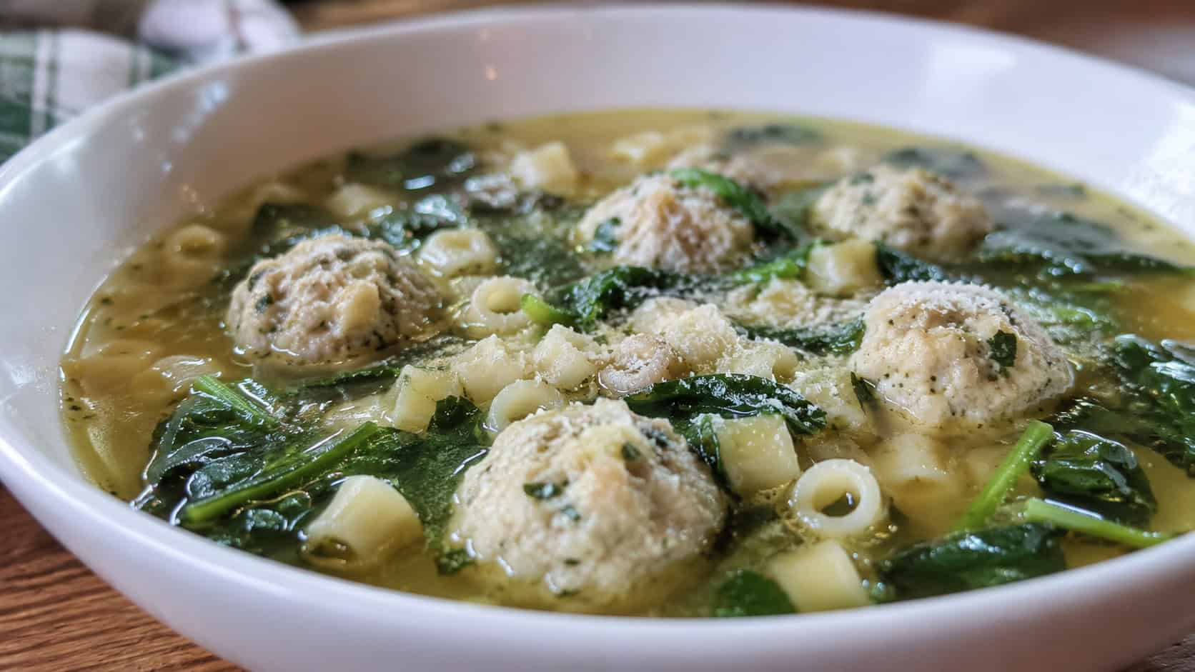 Italian wedding soup with little chicken meatballs, spinach, and tiny pasta in a clear broth in a wide horizontal shot in a bowl, a dusting of parmesan on top, natural light, shallow depth of field, landscape orientation