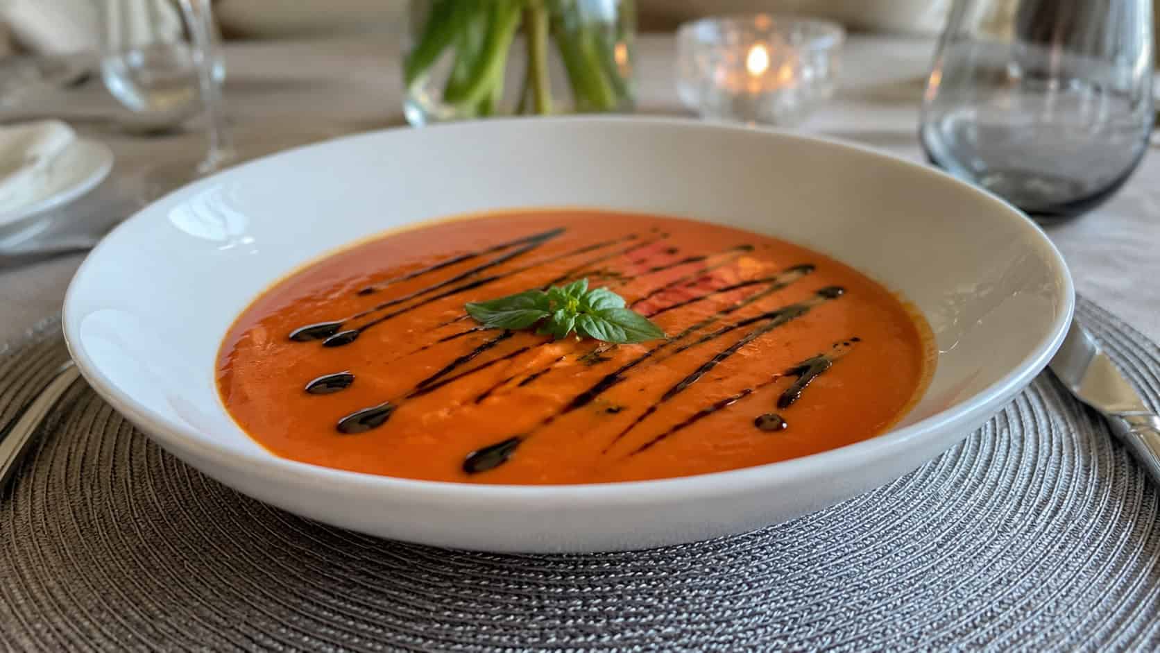 a creamy tomato soup in a wide white bowl with an artful drizzle of dark balsamic reduction across the top, in a wide horizontal shot, on an elegant table setting, natural light, shallow depth of field, landscape orientation