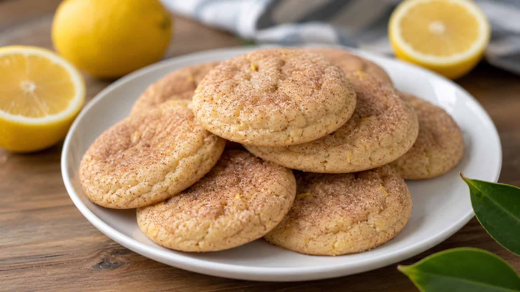 soft cinnamon cookies flecked with lemon zest and crackled cinnamon-sugar tops in a wide horizontal shot, on a bright plate with lemon halves nearby on a wooden table, fresh natural light, shallow depth of field, landscape orientation
