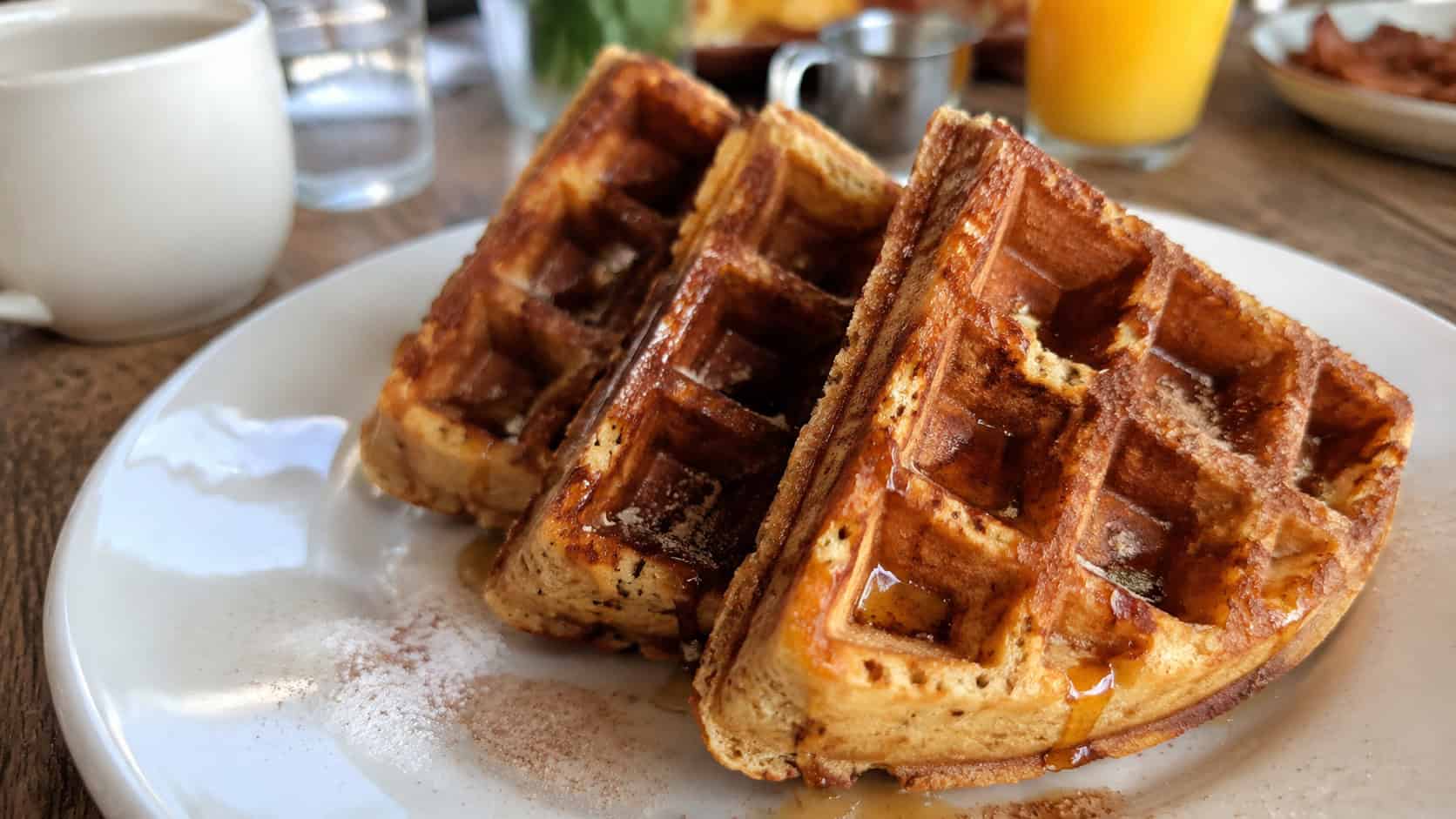crisp golden cinnamon waffles dusted with cinnamon sugar and drizzled with syrup in a wide horizontal shot, on a plate atop a wooden brunch table, bright natural light, shallow depth of field, landscape orientation