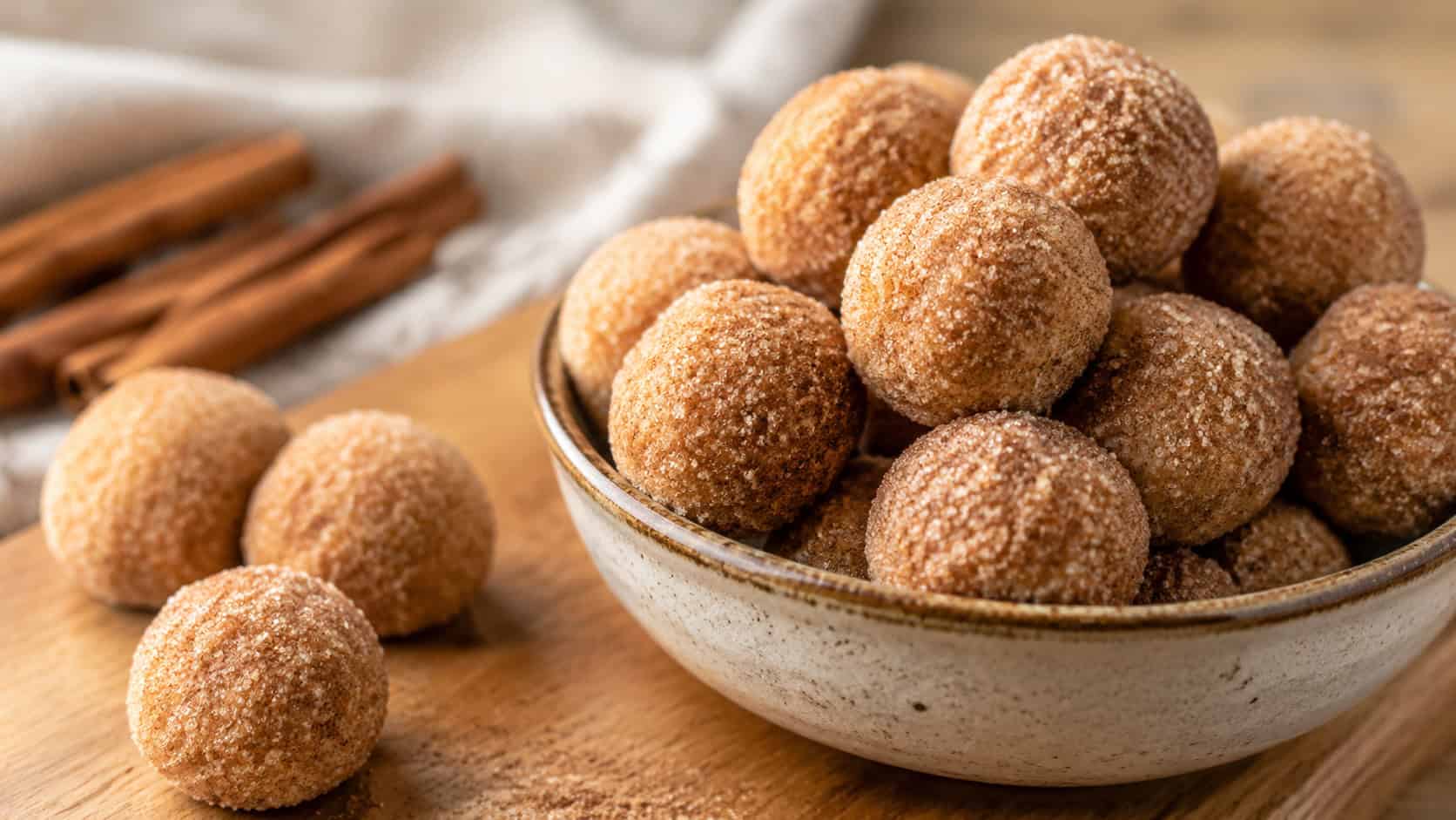 bite-size cinnamon cookie dough balls dusted with cinnamon sugar in a wide horizontal shot, piled in a small bowl with a few resting on a wooden board, warm natural light, shallow depth of field, landscape orientation