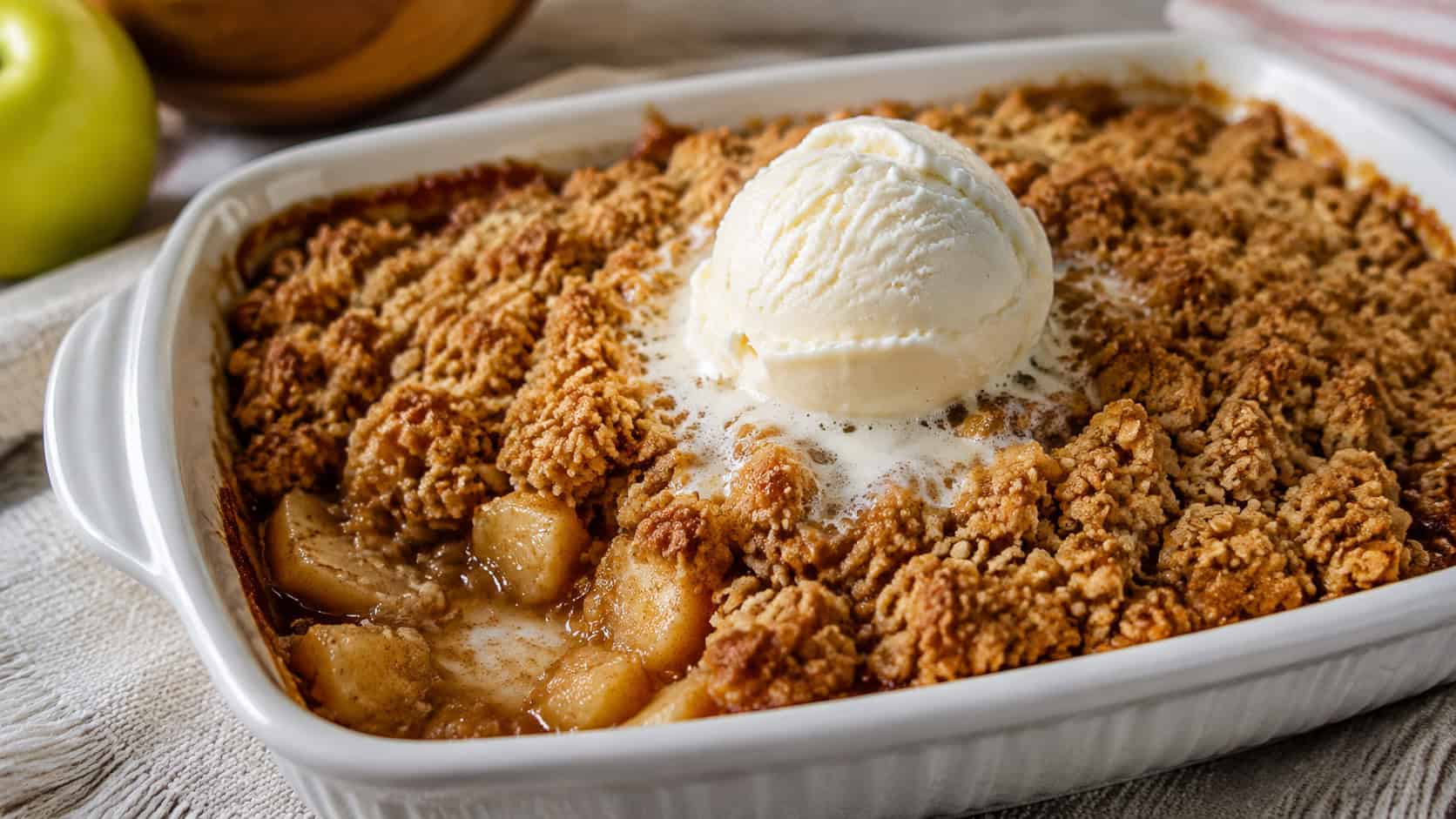a bubbling apple crisp with a golden cinnamon crumble topping in a wide horizontal shot, in a white baking dish with a scoop of vanilla ice cream melting on top, warm natural light, shallow depth of field, landscape orientation