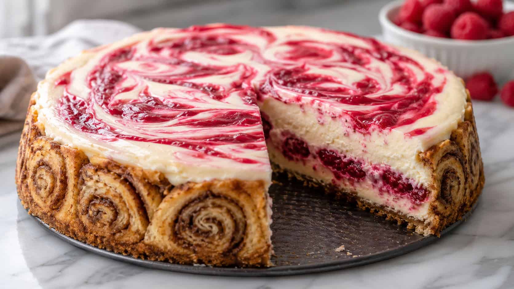 a raspberry cheesecake with a golden cinnamon-roll crust and ruby red sauce swirled on top, one slice revealing the layers, in a wide horizontal shot on a marble surface, natural light, shallow depth of field, landscape orientation