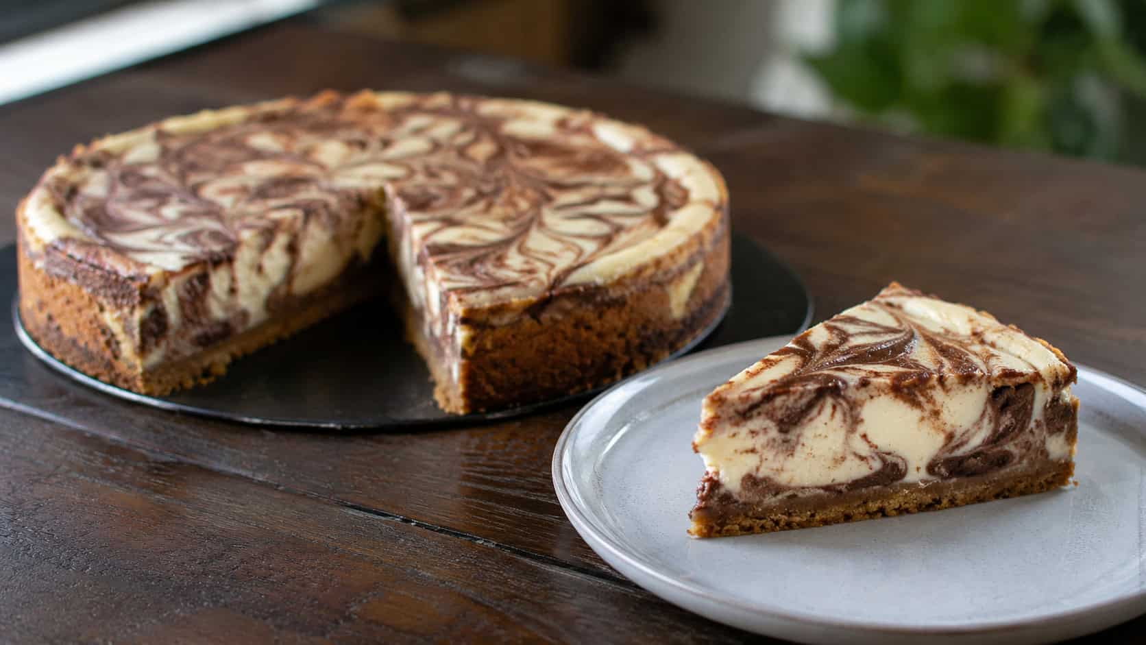 a cheesecake marbled with dark chocolate-hazelnut swirls and cinnamon ripples, one slice on a plate, in a wide horizontal shot on a dark wooden table, natural light, shallow depth of field, landscape orientation