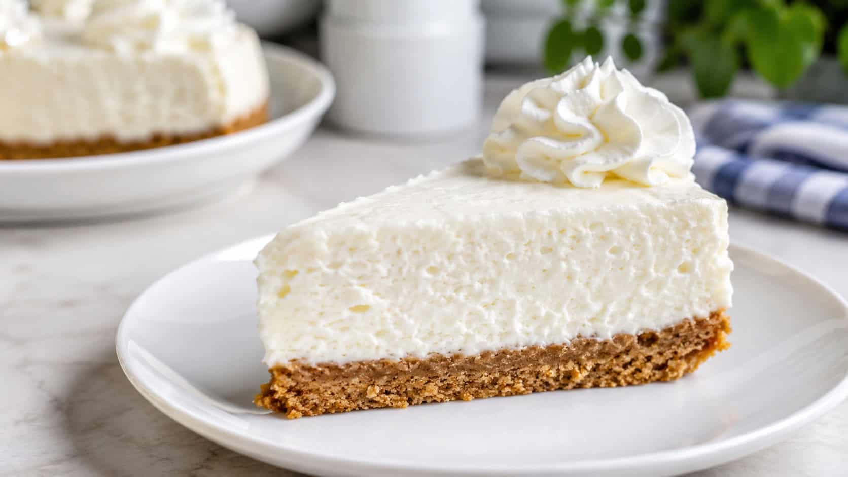 a fluffy no-bake vanilla cheesecake slice with a thick cookie crust on a white plate, soft swirl of cream on top, on a bright counter, wide horizontal shot, natural light, shallow depth of field, landscape orientation