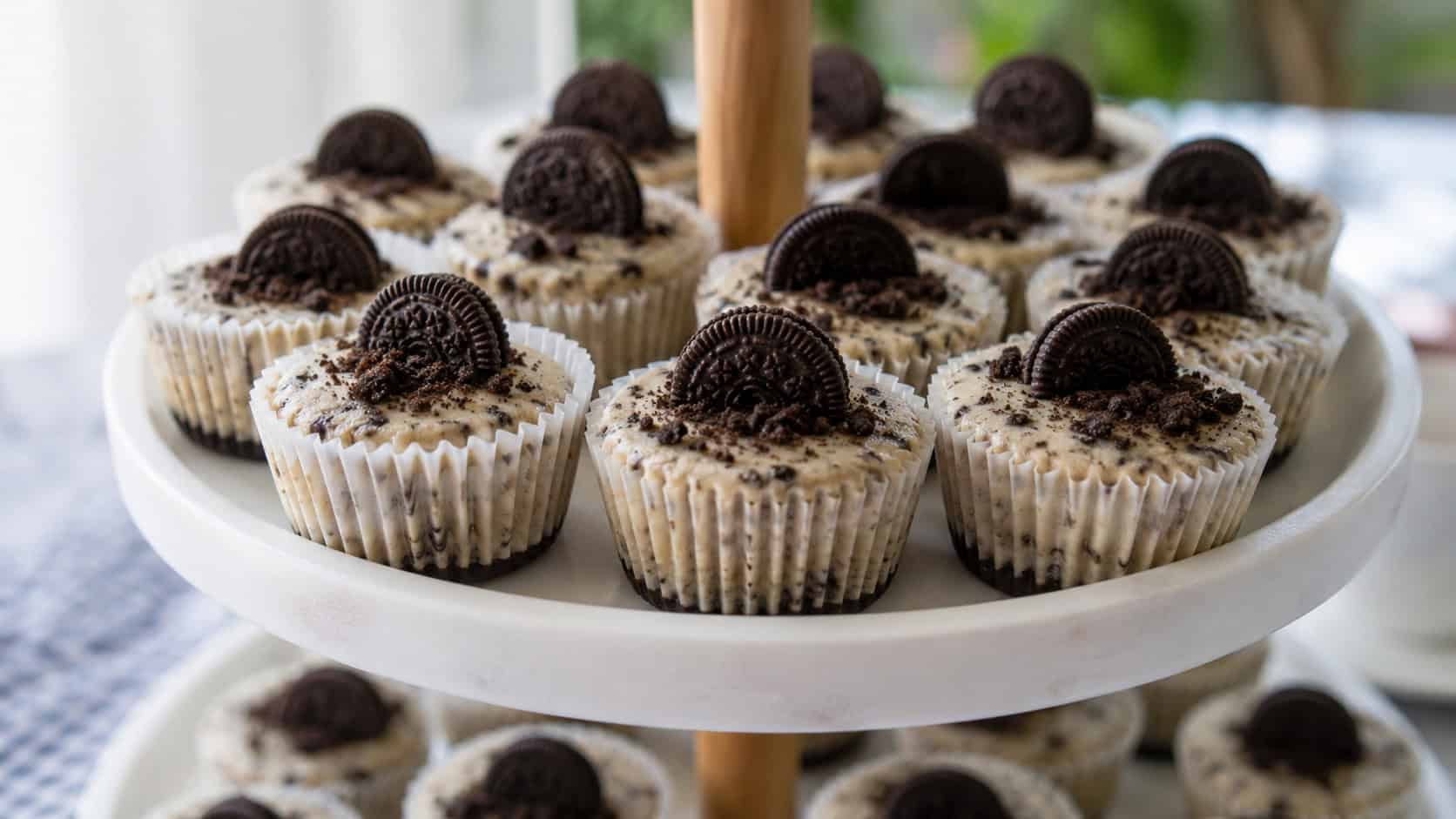 mini Oreo cheesecake bites in paper liners, topped with cookie crumbles and a small cookie piece, arranged on a tiered tray, wide horizontal shot, bright natural light, shallow depth of field, landscape orientation