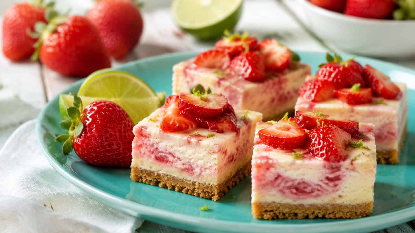 fresh strawberry lime cheesecake bars topped with juicy berries and lime zest on a turquoise plate in a wide horizontal shot, lime wedges and whole strawberries beside them, bright natural light, shallow depth of field, landscape orientation