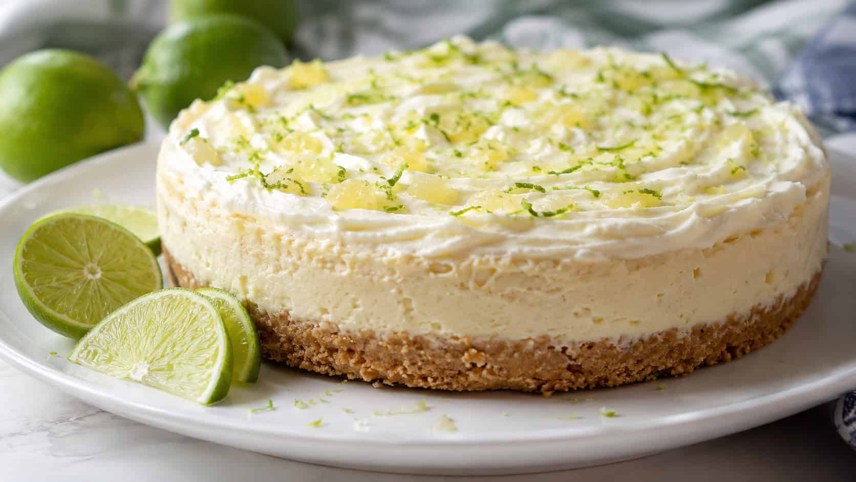 a pineapple lime cheesecake topped with lime zest and a creamy layer in a wide horizontal shot, on a bright plate with lime wedges, bright natural light, shallow depth of field, landscape orientation