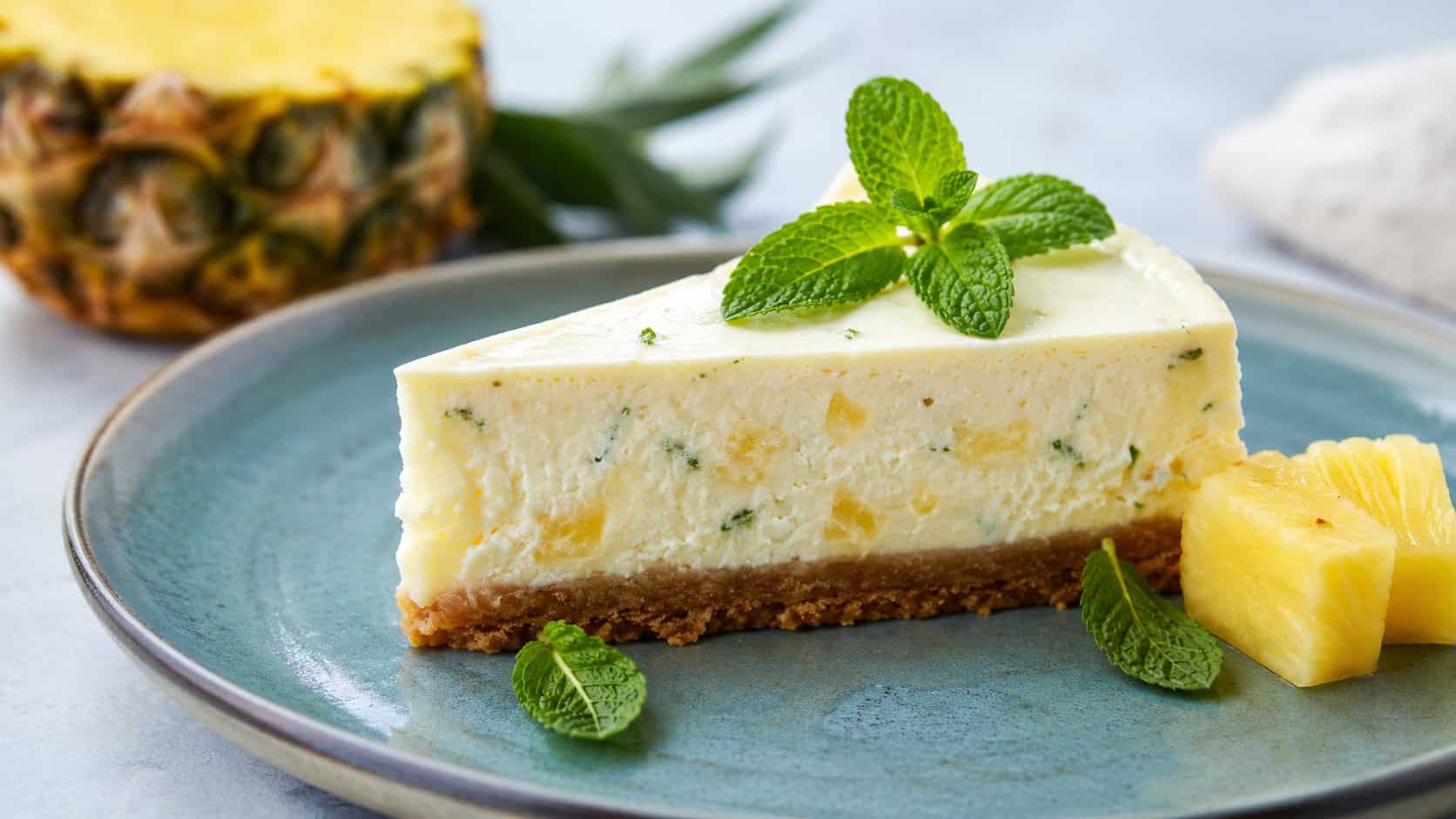 a pineapple mint cheesecake garnished with fresh mint leaves in a wide horizontal shot, on a cool-toned plate with pineapple, bright natural light, shallow depth of field, landscape orientation