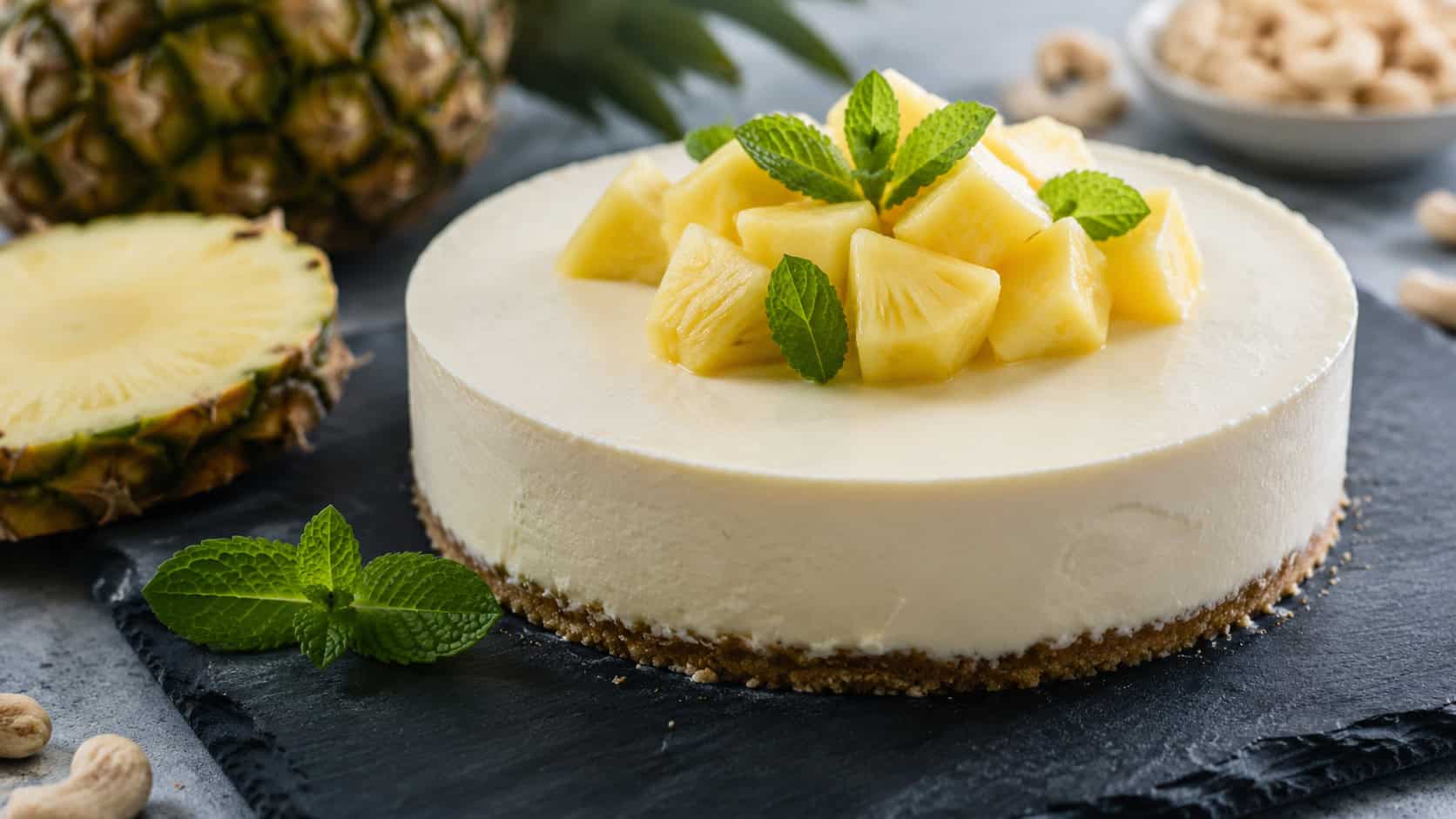 a smooth pale vegan pineapple cashew cheesecake in a wide horizontal shot, on a slate board with pineapple and mint, soft natural light, shallow depth of field, landscape orientation